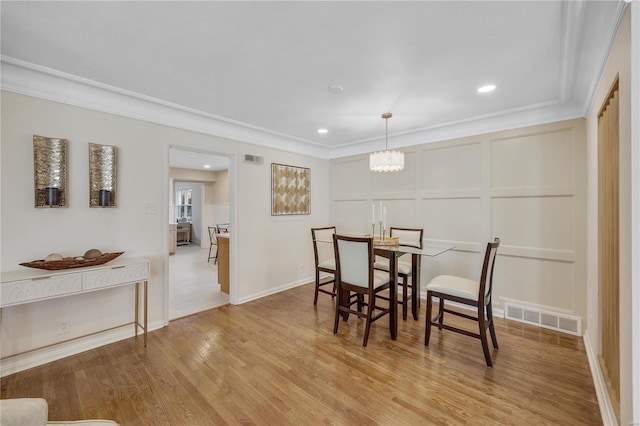 dining space featuring visible vents, a decorative wall, an inviting chandelier, light wood-style floors, and ornamental molding