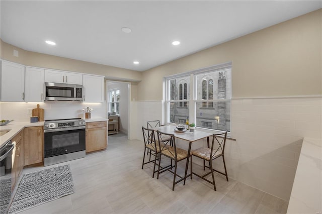 kitchen with brown cabinets, a wainscoted wall, stainless steel appliances, light countertops, and white cabinetry