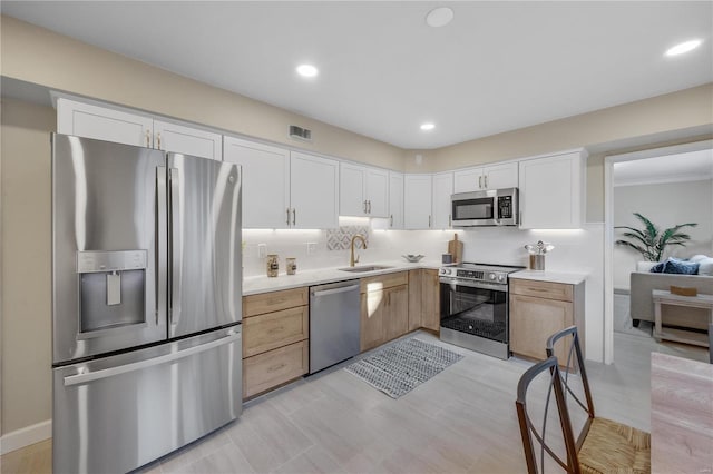 kitchen with white cabinets, decorative backsplash, stainless steel appliances, light countertops, and a sink