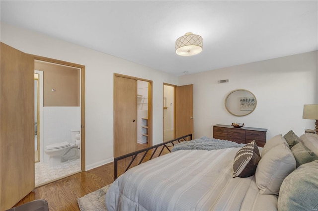 bedroom with a closet, visible vents, ensuite bathroom, wood finished floors, and baseboards