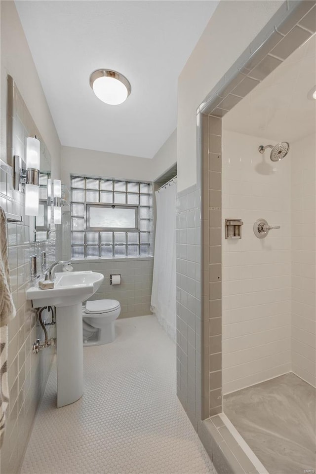 bathroom featuring tile walls, toilet, tile patterned flooring, a shower stall, and a sink