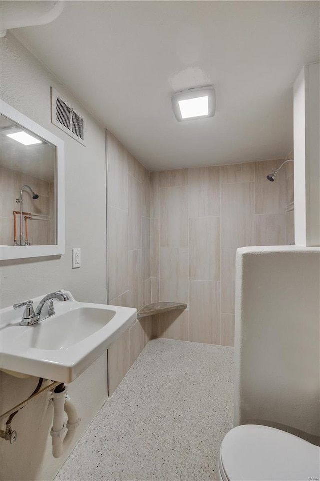 full bath featuring toilet, visible vents, a tile shower, and a sink