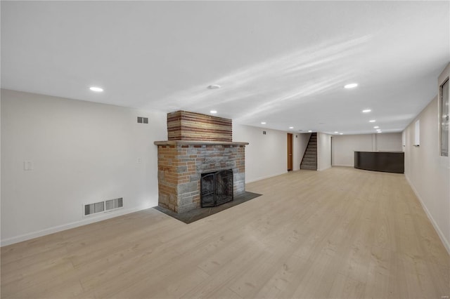 unfurnished living room with stairs, light wood-style flooring, a fireplace, and visible vents