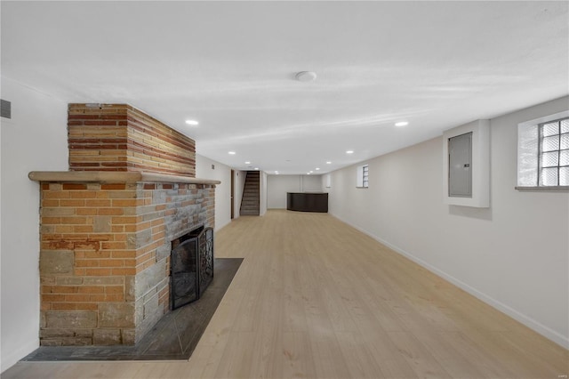 unfurnished living room featuring wood finished floors, visible vents, baseboards, a brick fireplace, and electric panel