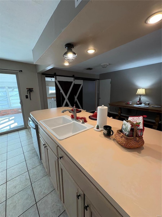 kitchen featuring a barn door, dishwasher, sink, and light tile patterned floors