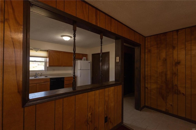 kitchen with black dishwasher, a textured ceiling, wooden walls, sink, and white fridge