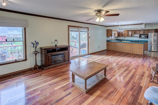 living room featuring a textured ceiling, light wood-type flooring, ceiling fan, and crown molding