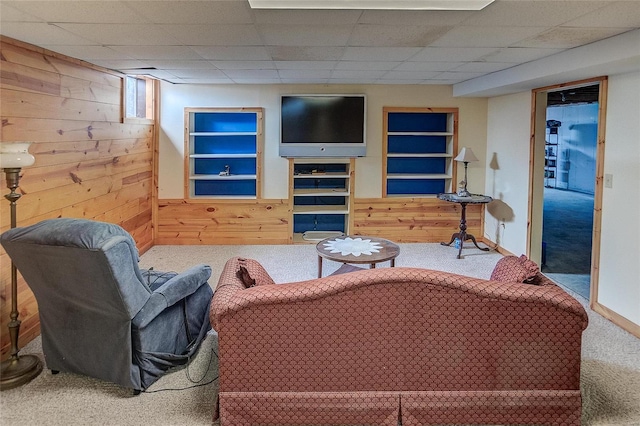 carpeted living room with a drop ceiling, built in features, and wood walls