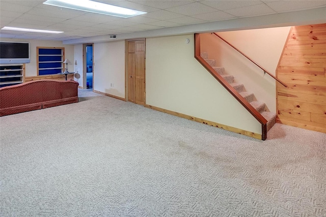 basement with a drop ceiling, carpet, and wood walls