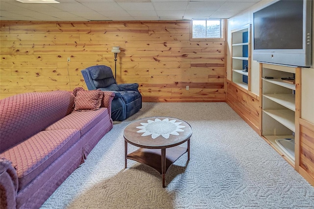 living area featuring wooden walls, a drop ceiling, and carpet flooring