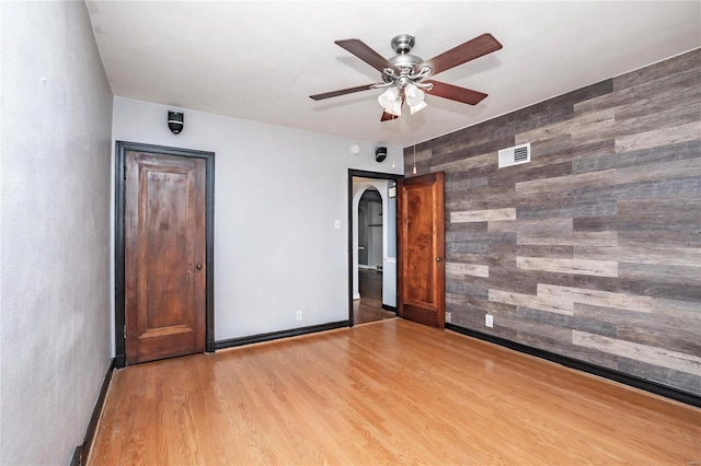 unfurnished room with wood walls, ceiling fan, and light hardwood / wood-style flooring