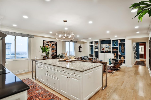 kitchen featuring ornamental molding, a kitchen island, white cabinetry, pendant lighting, and light hardwood / wood-style floors