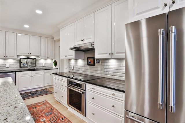 kitchen with stainless steel appliances, dark stone counters, white cabinets, backsplash, and light hardwood / wood-style flooring