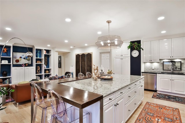 kitchen featuring hanging light fixtures, white cabinets, an island with sink, and dishwasher