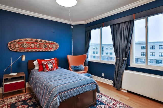 bedroom with hardwood / wood-style flooring, radiator heating unit, multiple windows, and crown molding