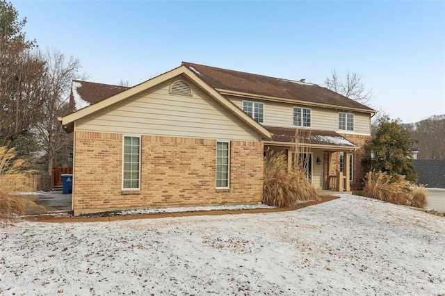 snow covered house featuring a porch and brick siding