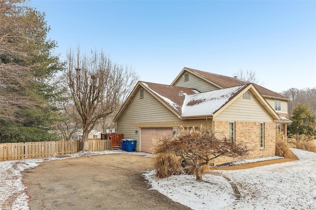 view of property exterior with an attached garage, driveway, fence, and brick siding