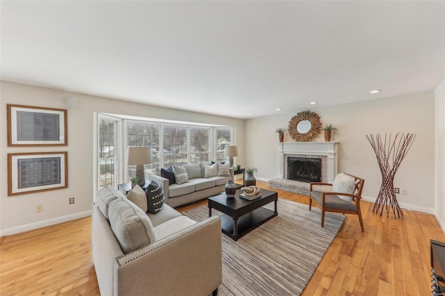 living area with recessed lighting, a brick fireplace, light wood-style flooring, and baseboards