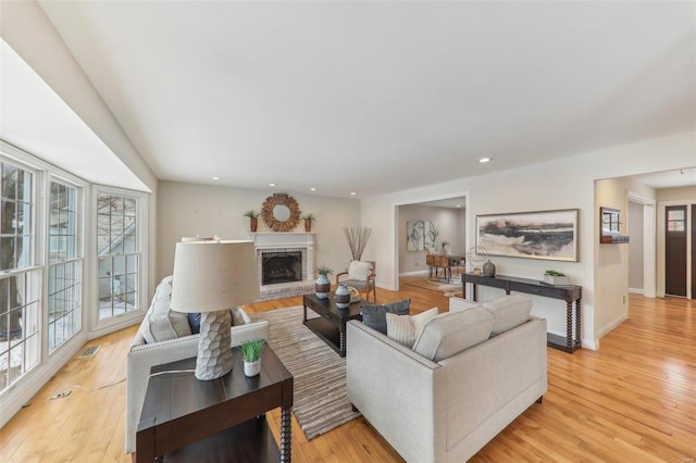 living room featuring light wood finished floors, a brick fireplace, and baseboards