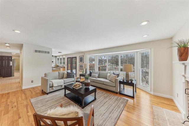 living area featuring a fireplace with flush hearth, light wood-type flooring, a wealth of natural light, and visible vents