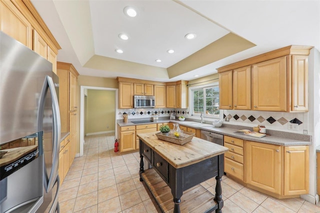 kitchen with a tray ceiling, wooden counters, backsplash, appliances with stainless steel finishes, and a sink