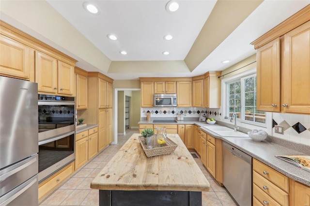 kitchen with stainless steel appliances, a sink, light countertops, a center island, and a raised ceiling