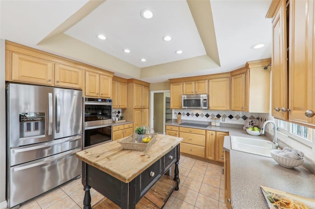 kitchen with light tile patterned floors, decorative backsplash, appliances with stainless steel finishes, a tray ceiling, and a sink