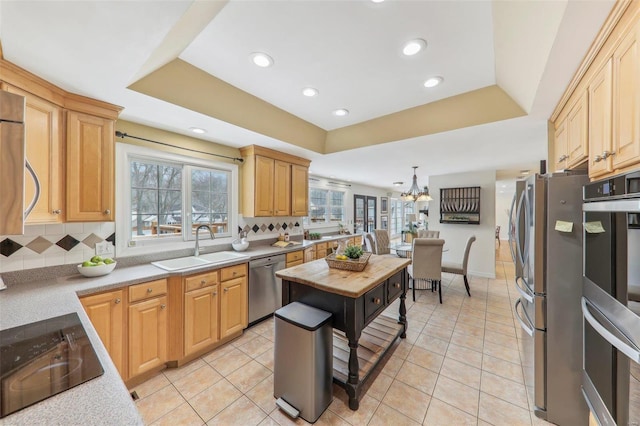 kitchen featuring a sink, appliances with stainless steel finishes, a raised ceiling, and pendant lighting