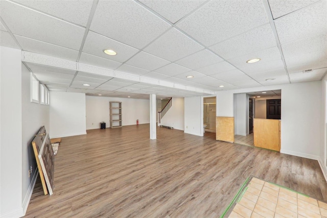 finished below grade area with a paneled ceiling, recessed lighting, stairway, wood finished floors, and baseboards