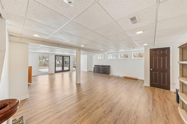 below grade area featuring french doors, a drop ceiling, light wood-style flooring, and baseboards