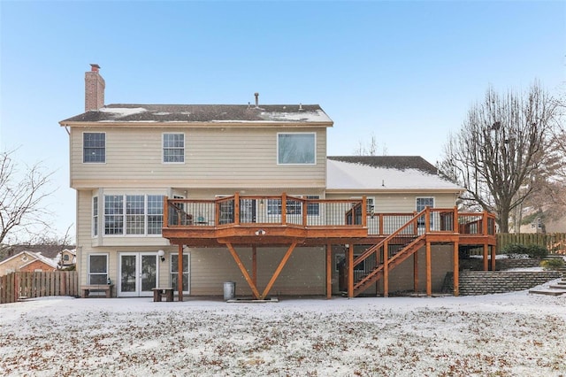 snow covered back of property with a deck, a chimney, stairs, and fence