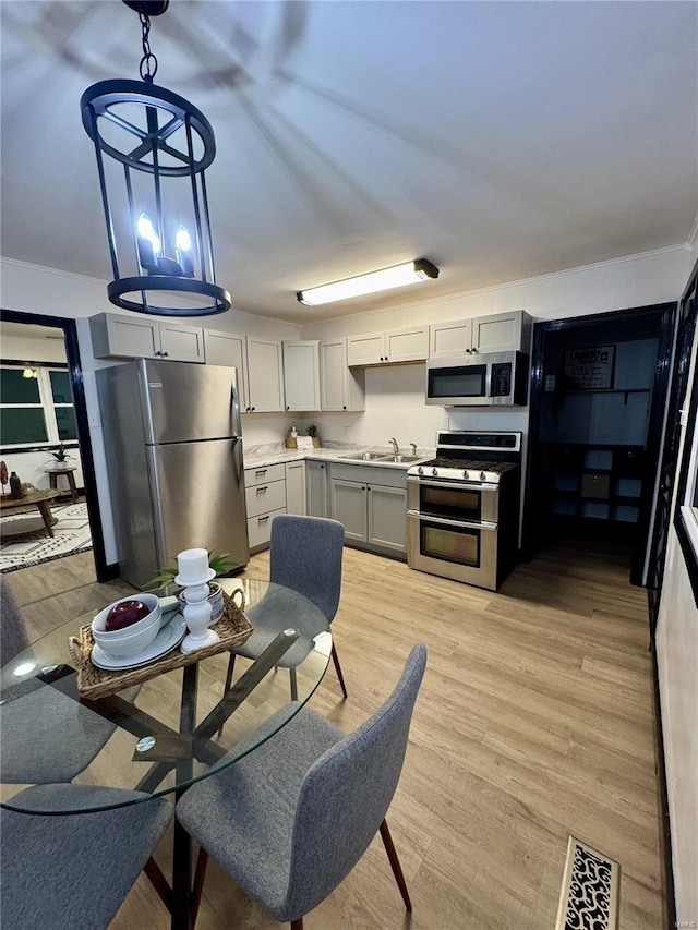 kitchen featuring gray cabinetry, sink, hanging light fixtures, light hardwood / wood-style flooring, and stainless steel appliances