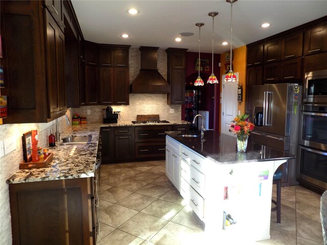 kitchen featuring sink, decorative light fixtures, custom range hood, and a kitchen island with sink