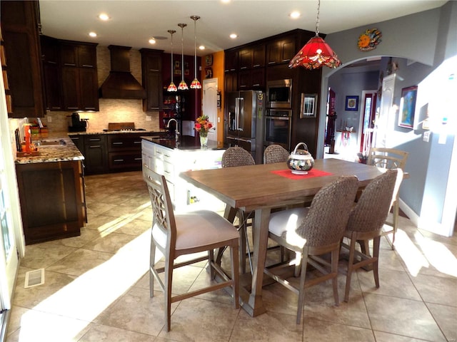 kitchen featuring pendant lighting, stainless steel appliances, custom exhaust hood, and an island with sink