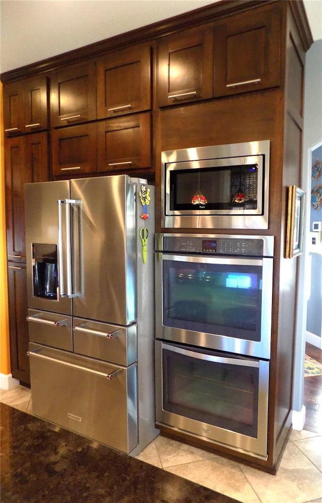 kitchen featuring stainless steel appliances, light tile patterned flooring, and dark stone countertops