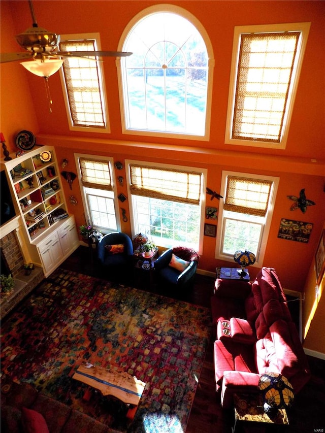 living room featuring a fireplace, wood-type flooring, ceiling fan, and a towering ceiling