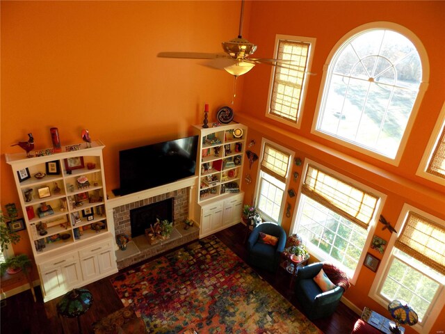 living room featuring ceiling fan, hardwood / wood-style floors, a brick fireplace, and a towering ceiling