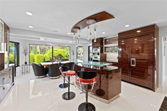 kitchen featuring stainless steel double oven, built in refrigerator, decorative light fixtures, a kitchen bar, and a kitchen island