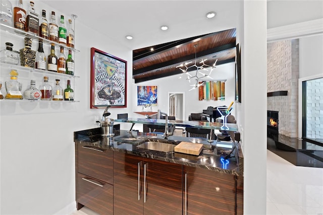 bar with beam ceiling, sink, dark stone counters, a fireplace, and light tile patterned floors