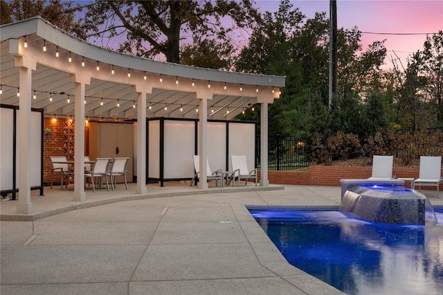 pool at dusk with pool water feature, a patio area, and a jacuzzi