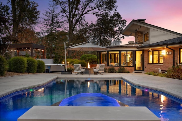 pool at dusk with a fire pit, a patio area, and an outdoor hot tub