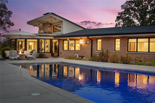 pool at dusk with a patio area and an outdoor fire pit