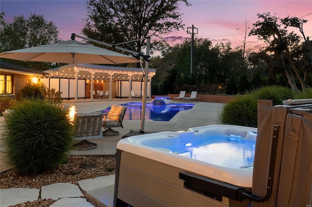 pool at dusk with a hot tub and a patio area