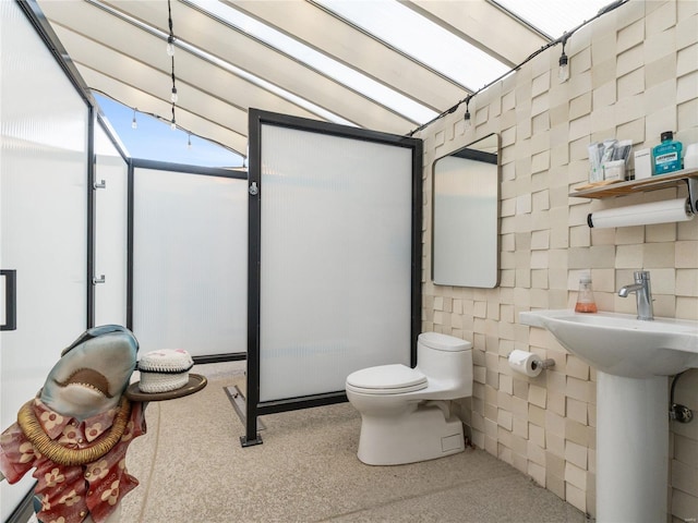 bathroom featuring toilet, vaulted ceiling, tile walls, and sink