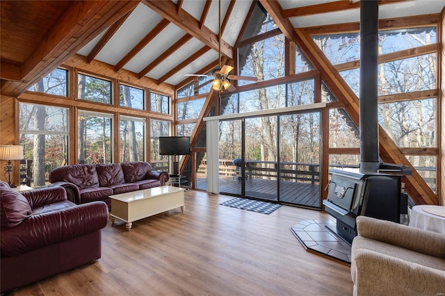 living room with a wood stove, high vaulted ceiling, ceiling fan, beamed ceiling, and light hardwood / wood-style floors