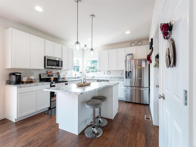 kitchen with white cabinets, stainless steel appliances, hanging light fixtures, and dark hardwood / wood-style floors