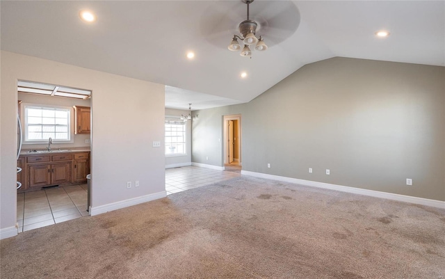 carpeted spare room with ceiling fan with notable chandelier, a healthy amount of sunlight, lofted ceiling, and sink