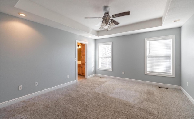 carpeted spare room with ceiling fan and a raised ceiling