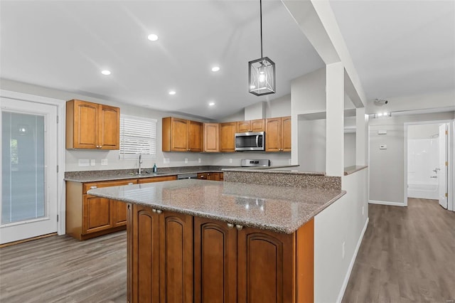 kitchen featuring light stone countertops, vaulted ceiling, pendant lighting, light hardwood / wood-style flooring, and sink