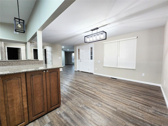 kitchen with decorative light fixtures, dark wood-type flooring, light stone counters, and dark brown cabinets